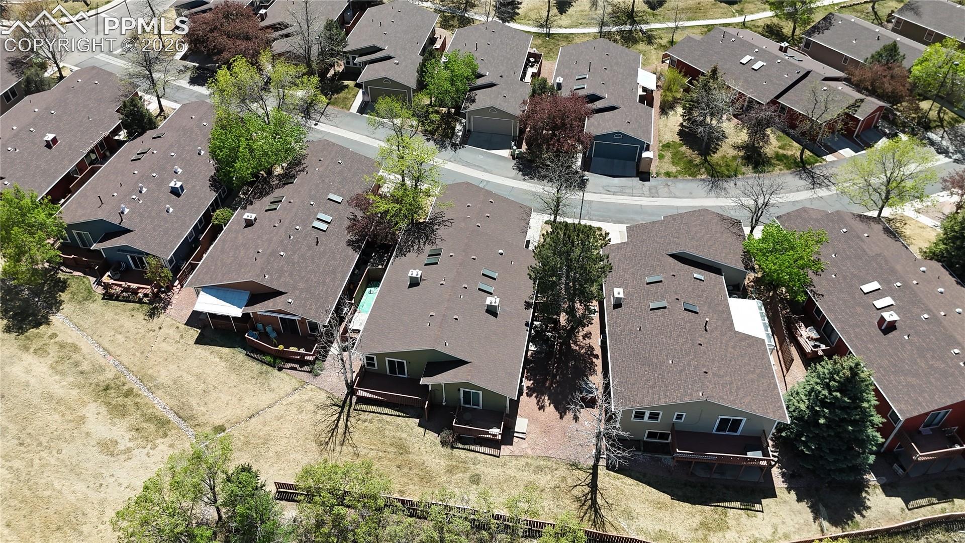Aerial view of the property and its surrounding neighborhood, featuring residential homes with brown roofs, green landscaping, and paved streets
