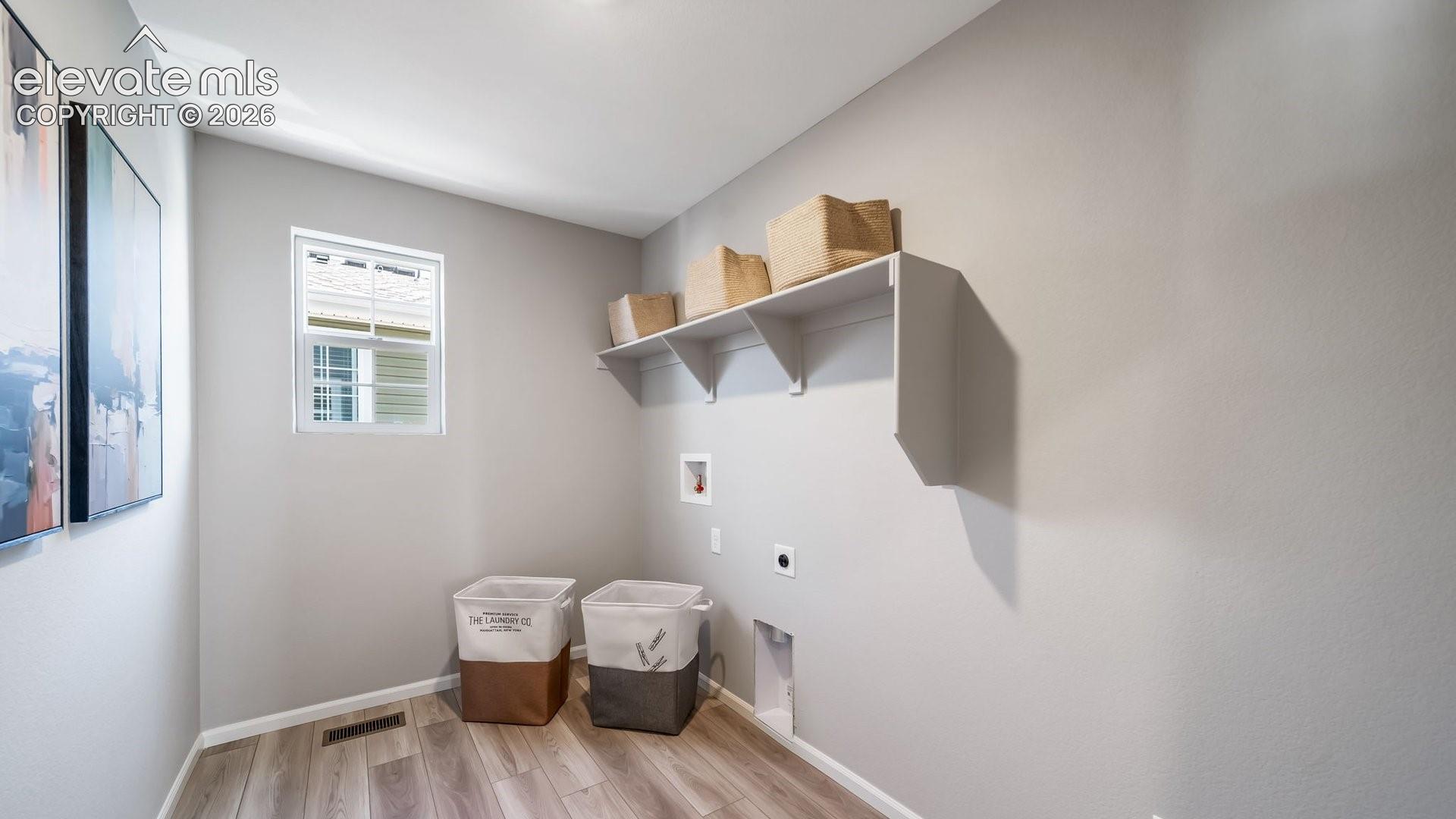 Dedicated utility space featuring wood-finish flooring, a white-framed window, and integrated wall shelving
*photos of a model home*