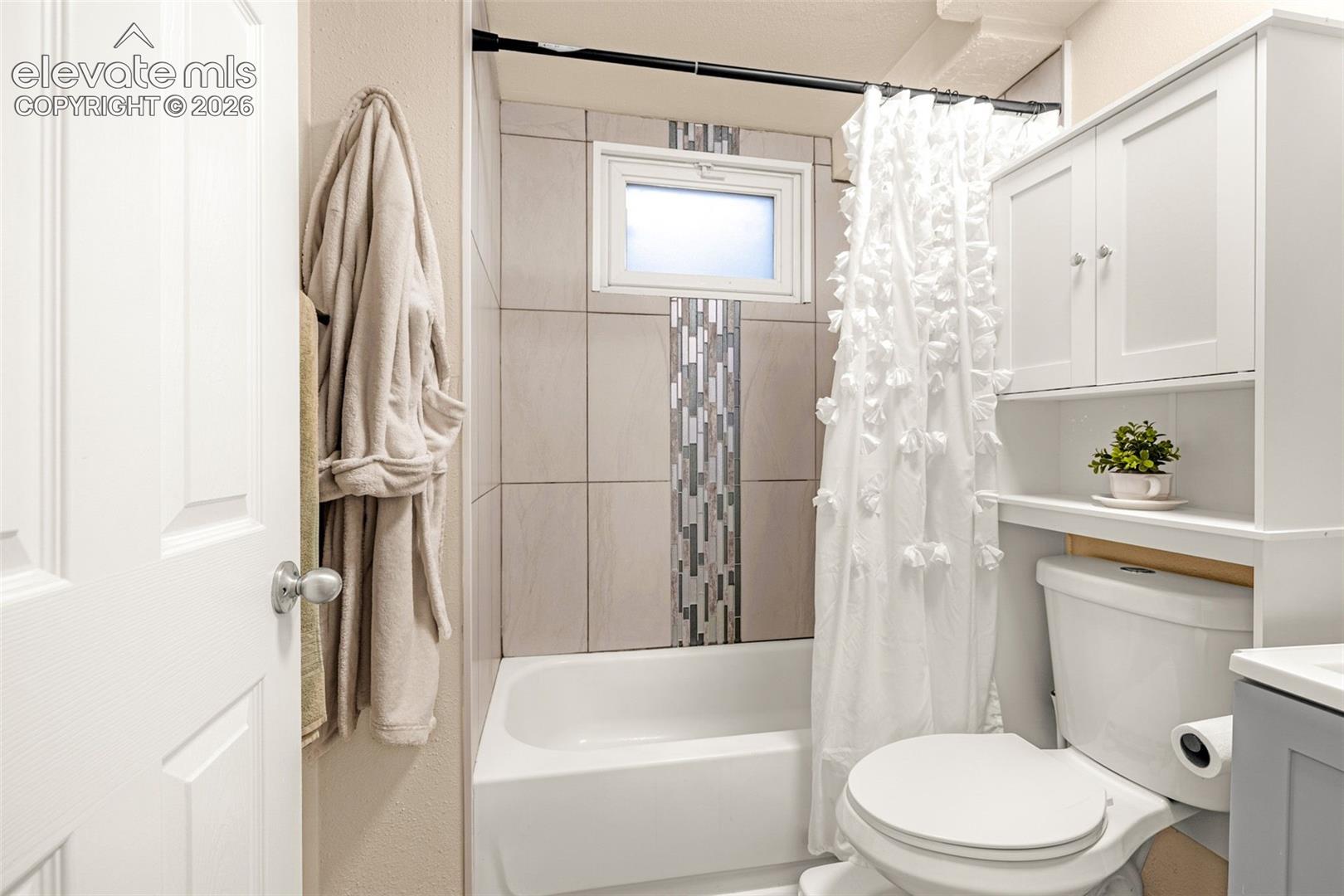 White bathtub and shower combination with a tile surround, mosaic accent strip, and a window