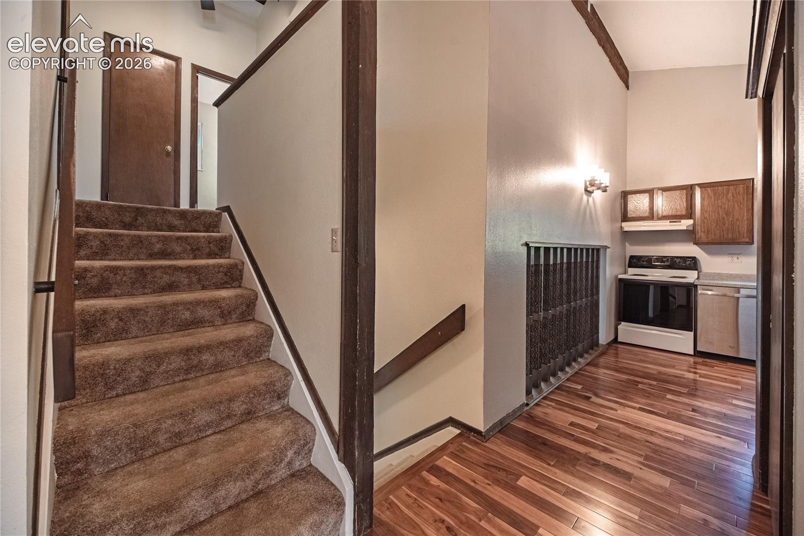 Carpeted staircase featuring wood trim, wood-finish flooring, metal railing, and built-in cabinetry