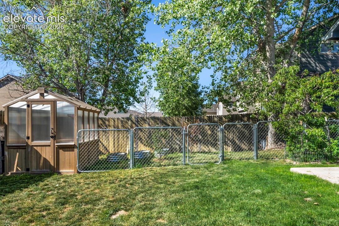 Backyard featuring a wood-frame greenhouse, chain-link perimeter fencing, and mature trees