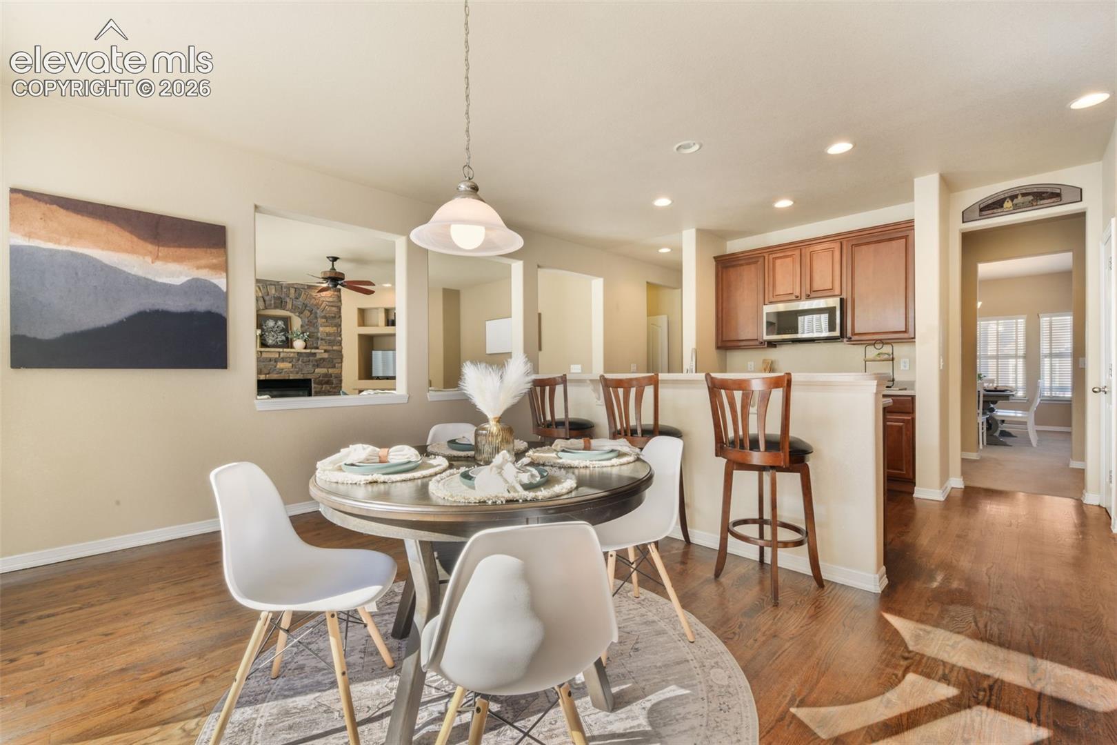 Hardwood-finish flooring, recessed lighting, kitchen with rich wood cabinetry, stainless steel microwave, and a pass-through window to an additional living space