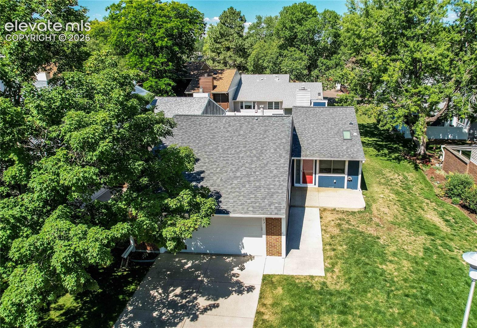 Residential exterior featuring a pitched shingle roof, concrete driveway, attached garage, and mature trees on the lot