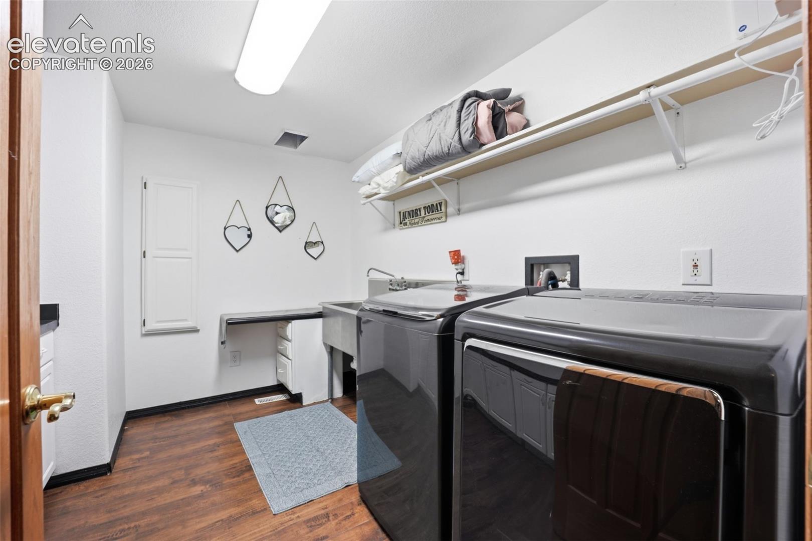 Laundry area featuring wood-finish flooring, a utility sink, and built-in shelving