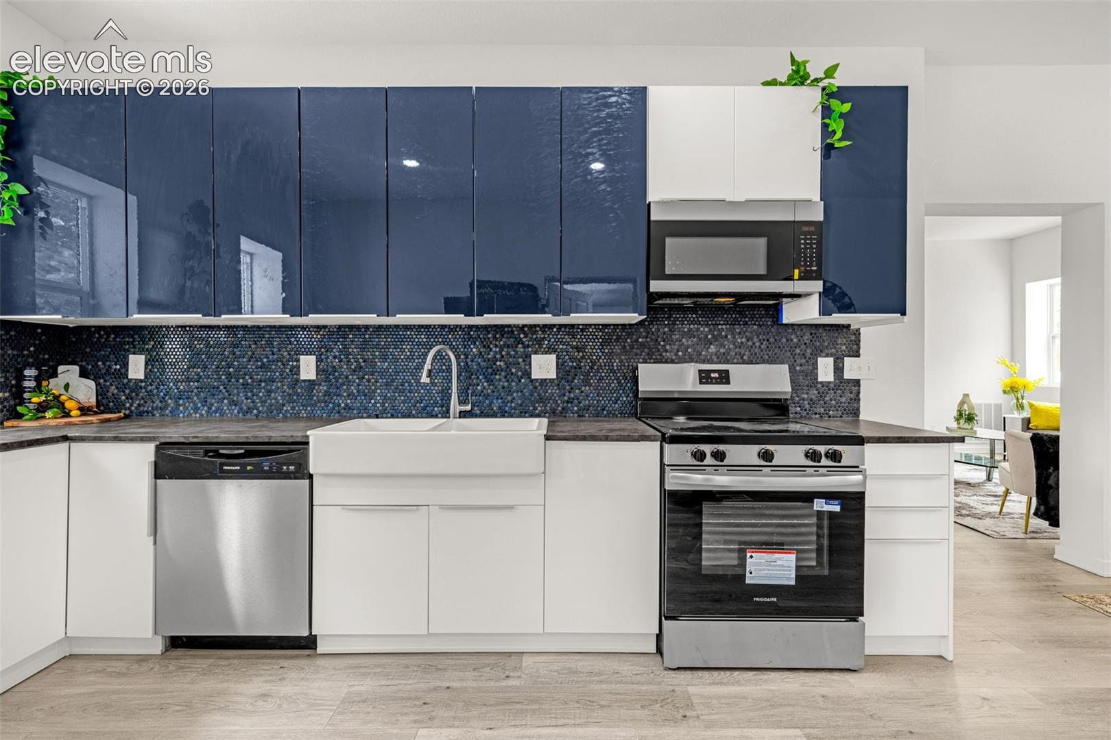 Modern kitchen featuring gloss navy and white cabinetry, a white farmhouse sink, stainless steel appliances, and a dark stone-finish countertop