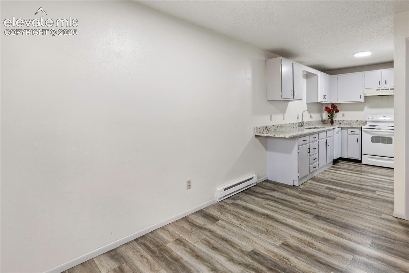 Kitchen featuring white cabinetry, light-toned countertops, a stainless steel sink, and white appliances including a range and overhead microwave