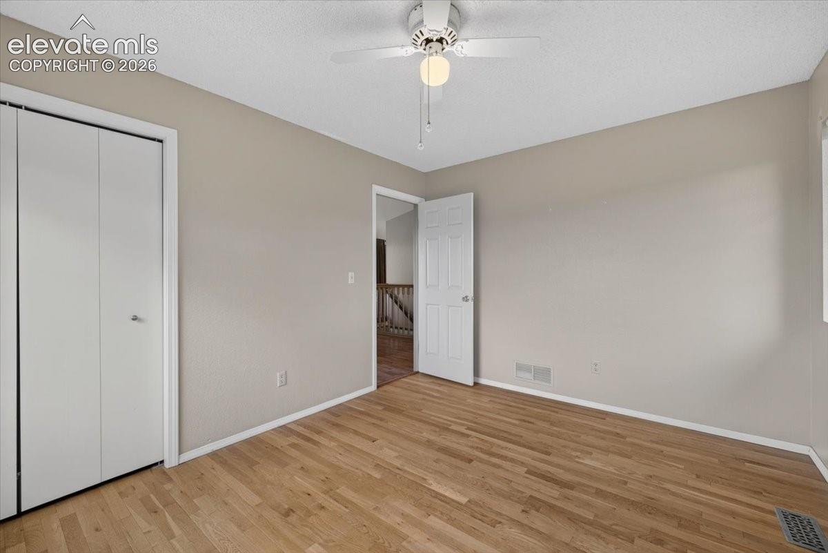 Main level bedroom featuring wood-finish flooring, ceiling fan with integrated lighting, and white six-panel door