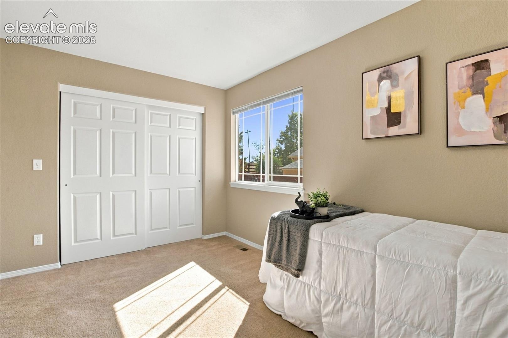 Neutral tone wall paint with white trim, double pane window, carpeted flooring, and a closet with paneled bi-fold doors