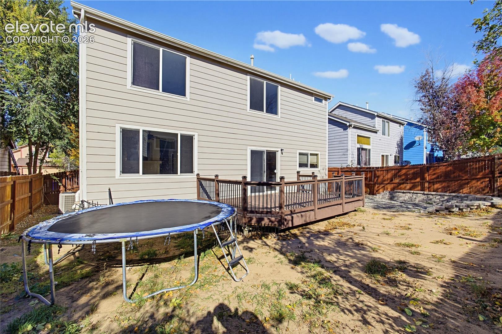 Two-story exterior with horizontal siding, elevated rear deck with metal balusters, and a backyard enclosed by wooden privacy fencing