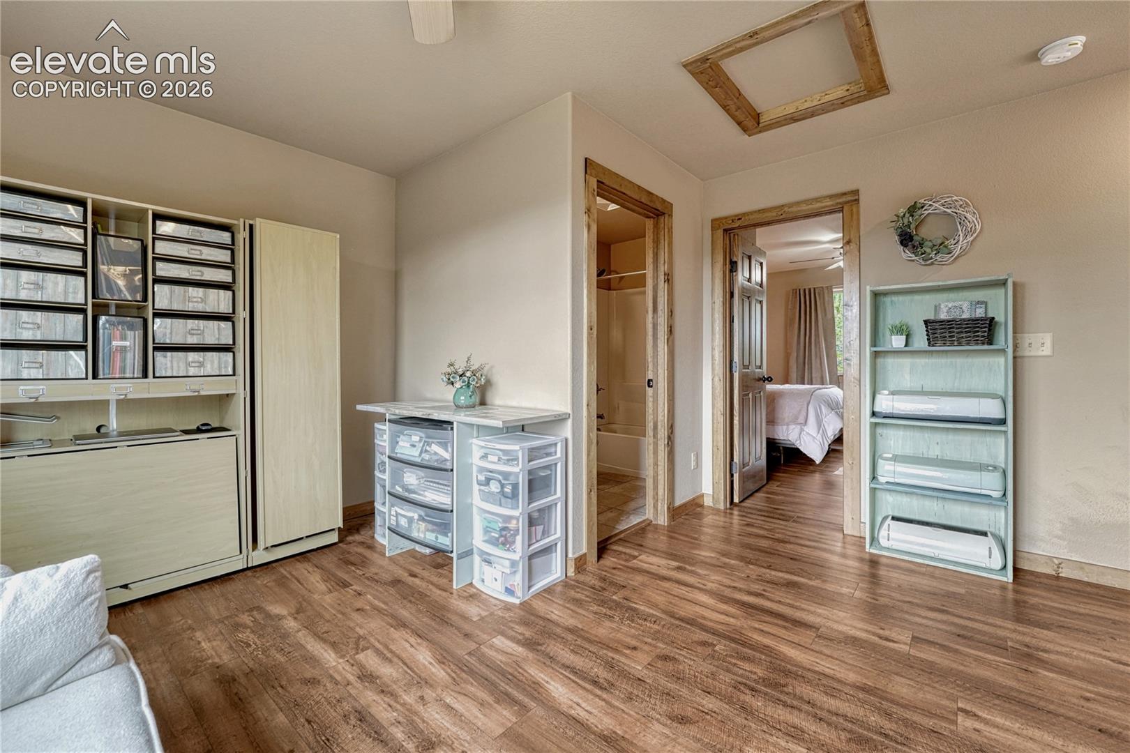 Wood-finish flooring, built-in storage cabinetry, wood-trimmed door frames, and a ceiling attic access panel