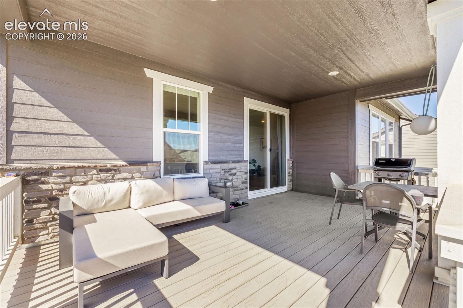 Covered deck featuring composite decking, horizontal siding, stone veneer accents, and a sliding glass door
