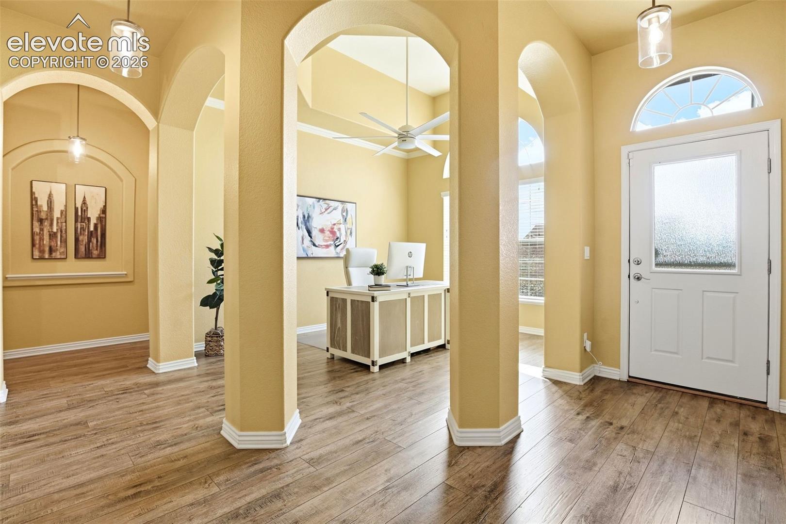Wood-finish flooring, arched doorways, recessed wall panels, a transom window, and a tray ceiling