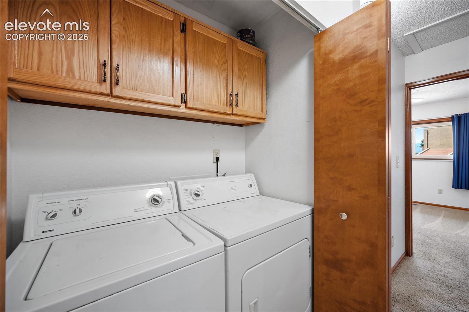 Dedicated laundry area featuring white appliances and wood cabinetry with metal hardware