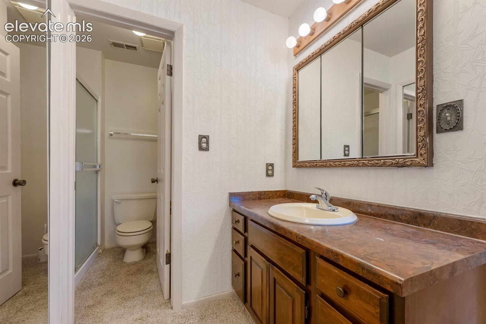 Bathroom featuring a wood-finish vanity with a molded countertop and integrated sink, a multi-panel medicine cabinet, and a walk-in shower stall with an opaque glass door