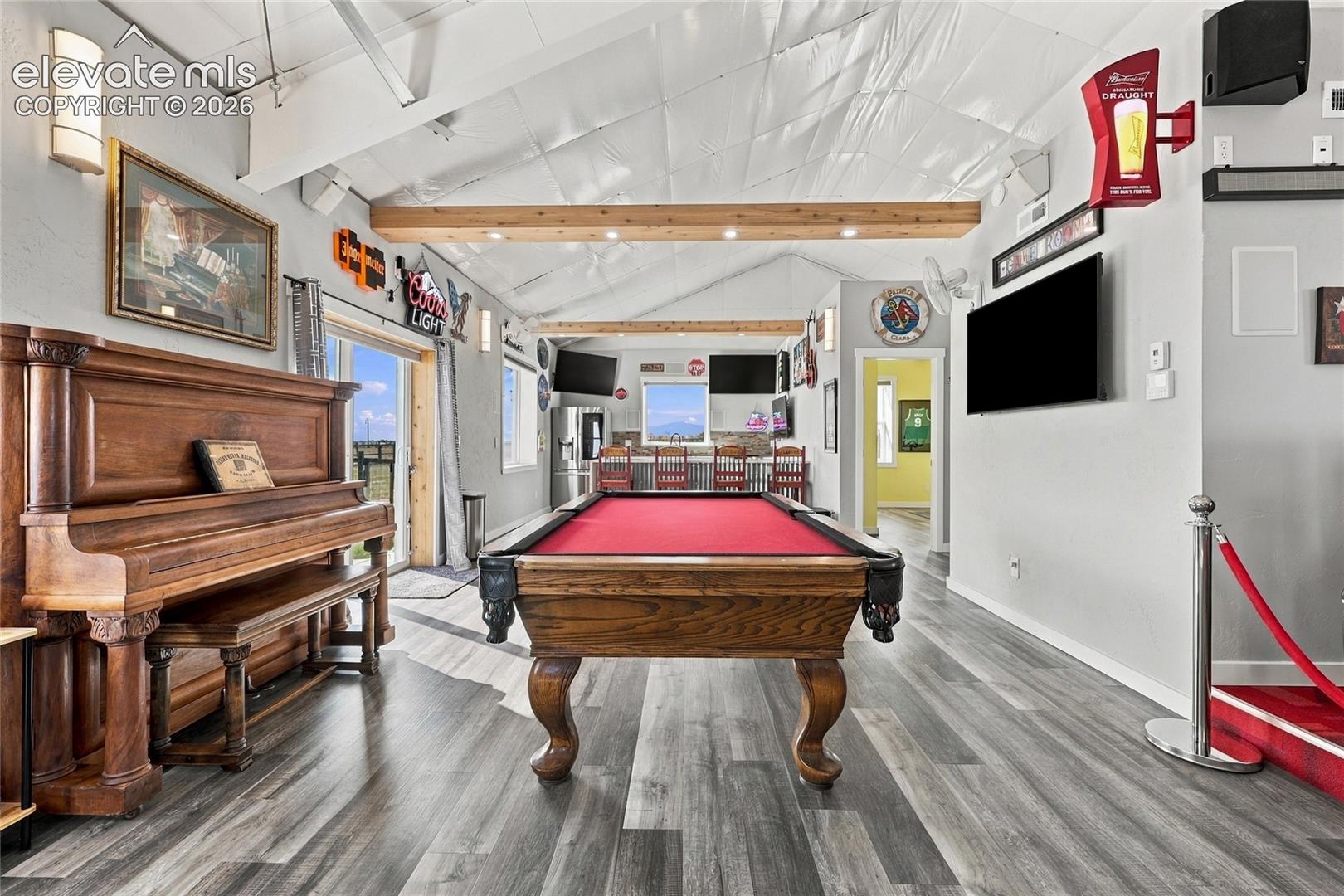 Vaulted ceiling featuring exposed timber beams, wood-finish flooring, and a built-in wet bar with stone-texture detailing