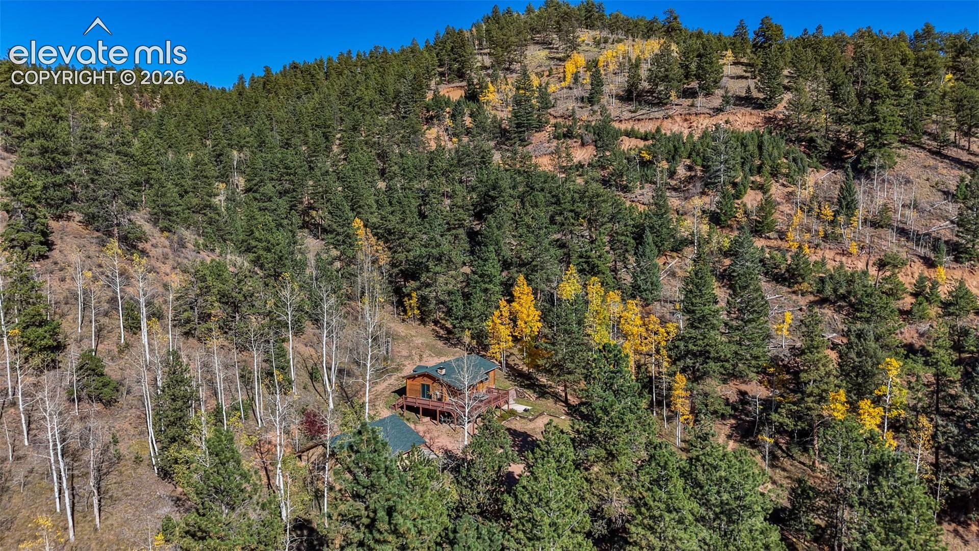 Aerial perspective of a wood-sided structure situated on a sloped lot featuring a dense concentration of mature pine and aspen trees