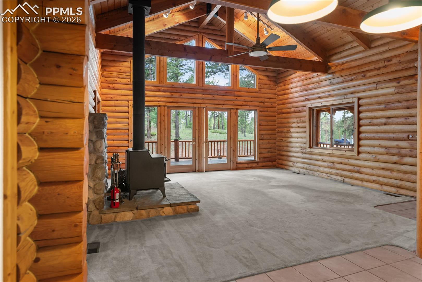 Unfurnished living room featuring a wood stove, log walls, high vaulted ceiling, a wooden ceiling with exposed beams, and carpet