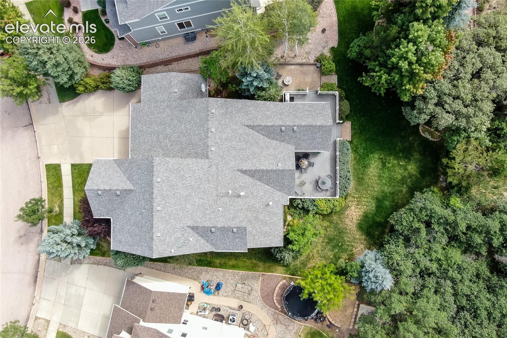 Aerial perspective of a property featuring an expansive lawn, mature tree canopy, concrete driveway, and a rear deck.