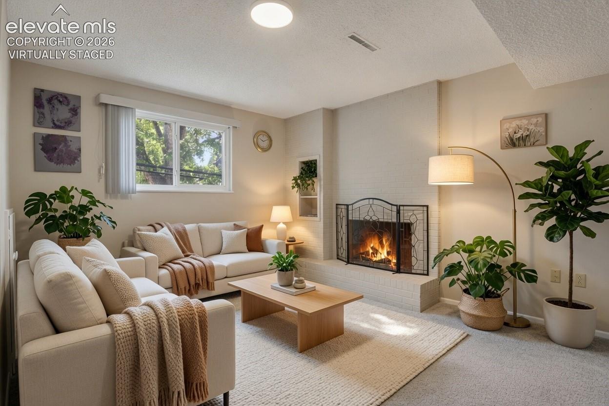 Virtually staged living room with a wood-burning fireplace with decorative surround, neutral upholstered seating, wood-finish coffee table, recessed ceiling lighting, and large multi-pane windows allowing natural light