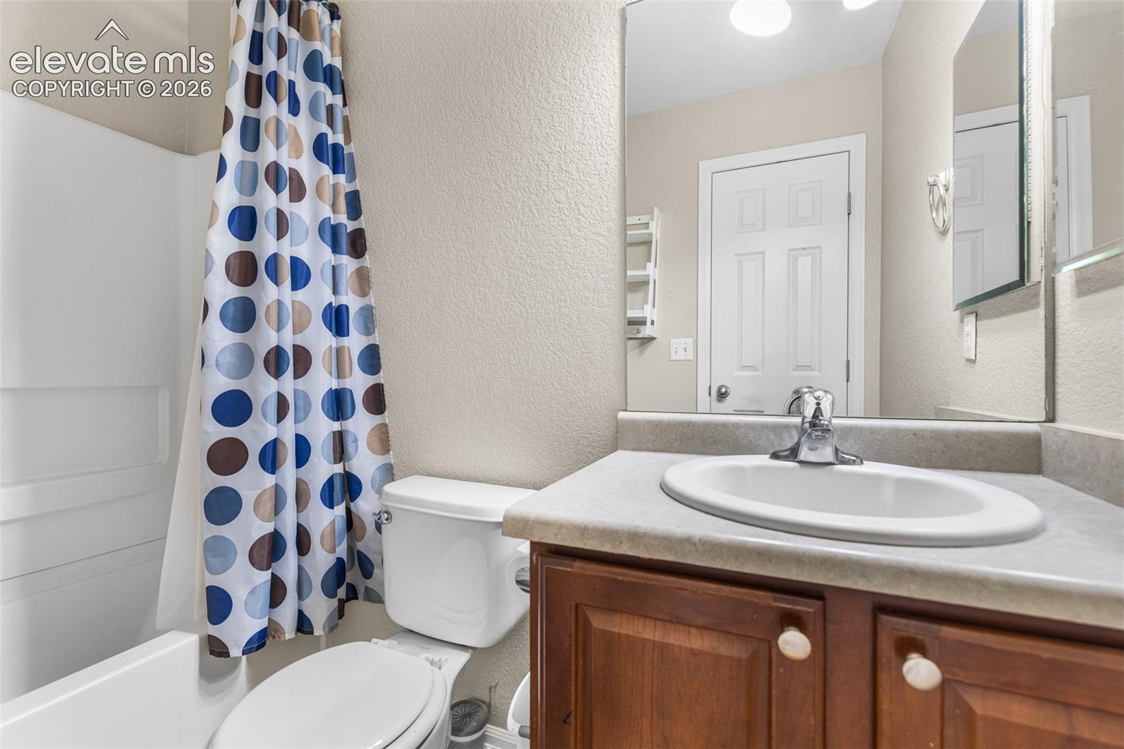 Bathroom featuring wood-finish vanity cabinetry, integrated countertop with oval basin, chrome faucet, wall-mounted mirror, and tub-shower combination with surround