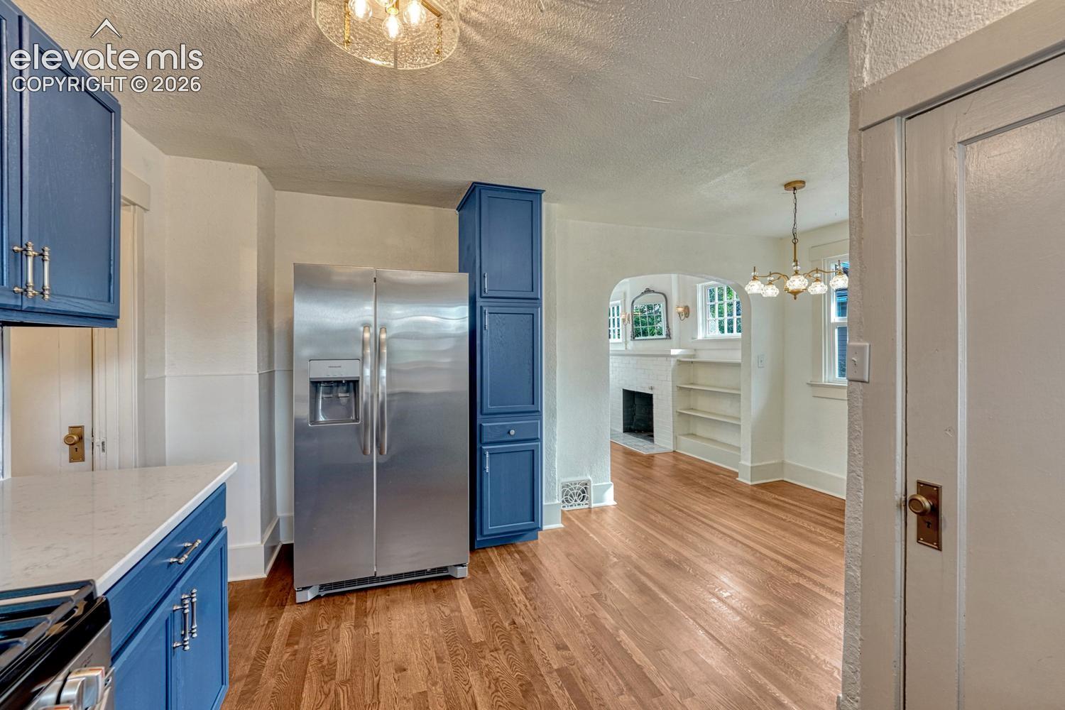 Wood-finish flooring, blue cabinetry with silver-tone hardware, stainless steel refrigerator, arched doorway, and built-in shelving