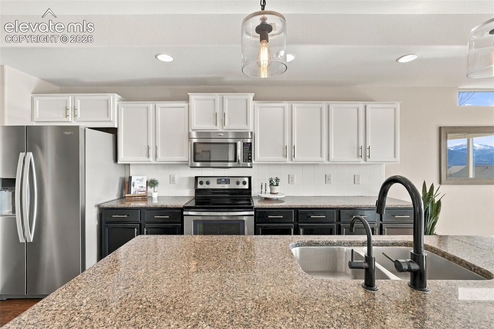 Kitchen featuring two-tone cabinetry, stone countertops, stainless steel appliances, a double-basin undermount sink with a matte black faucet, and pendant lighting