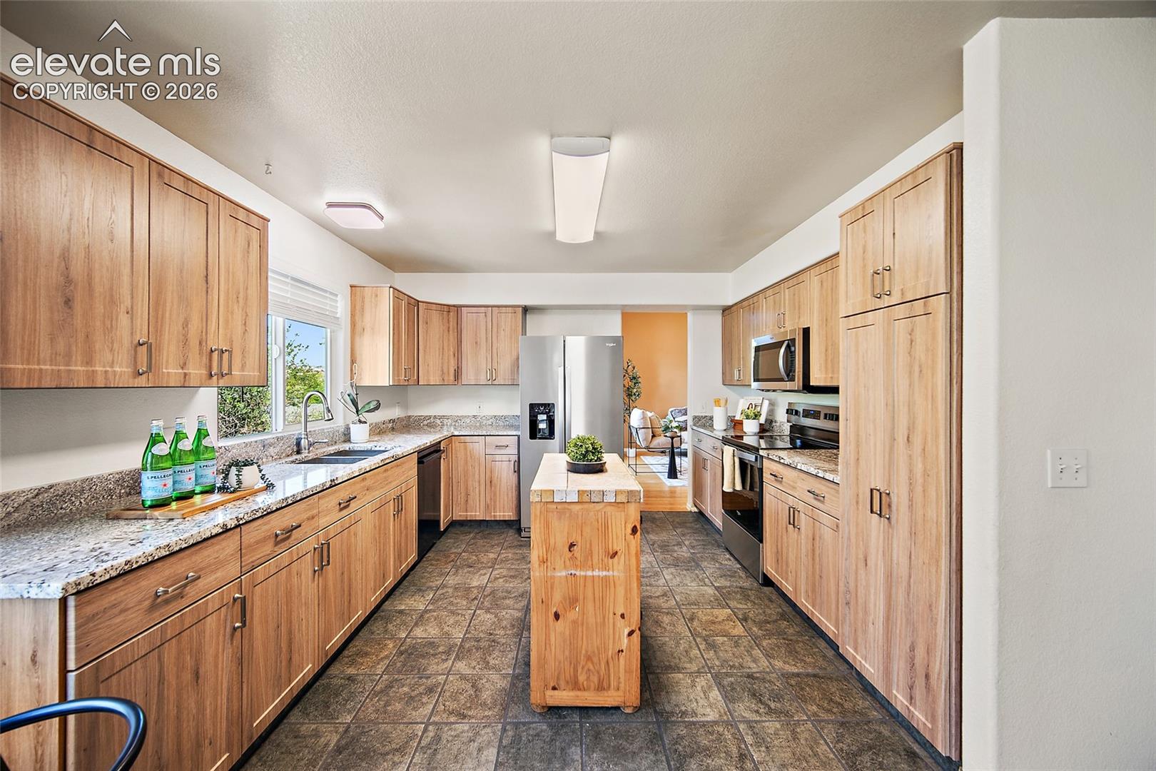 Kitchen featuring wood-finish cabinetry, granite countertops, stainless steel appliances, a center island with a butcher block top, and tiled flooring
