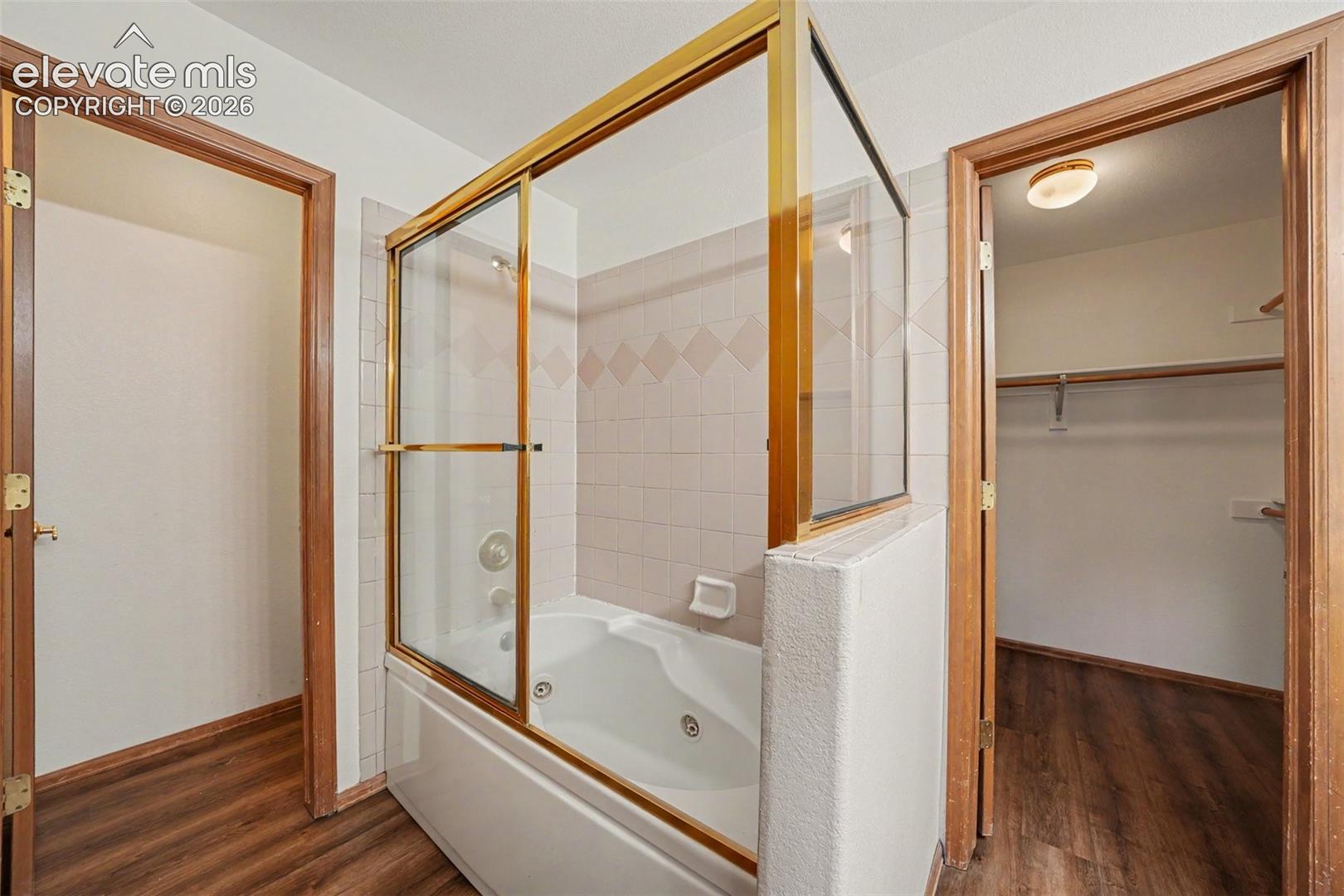 Jetted tub with gold-finish sliding glass enclosure, white tile surround, and built-in jets