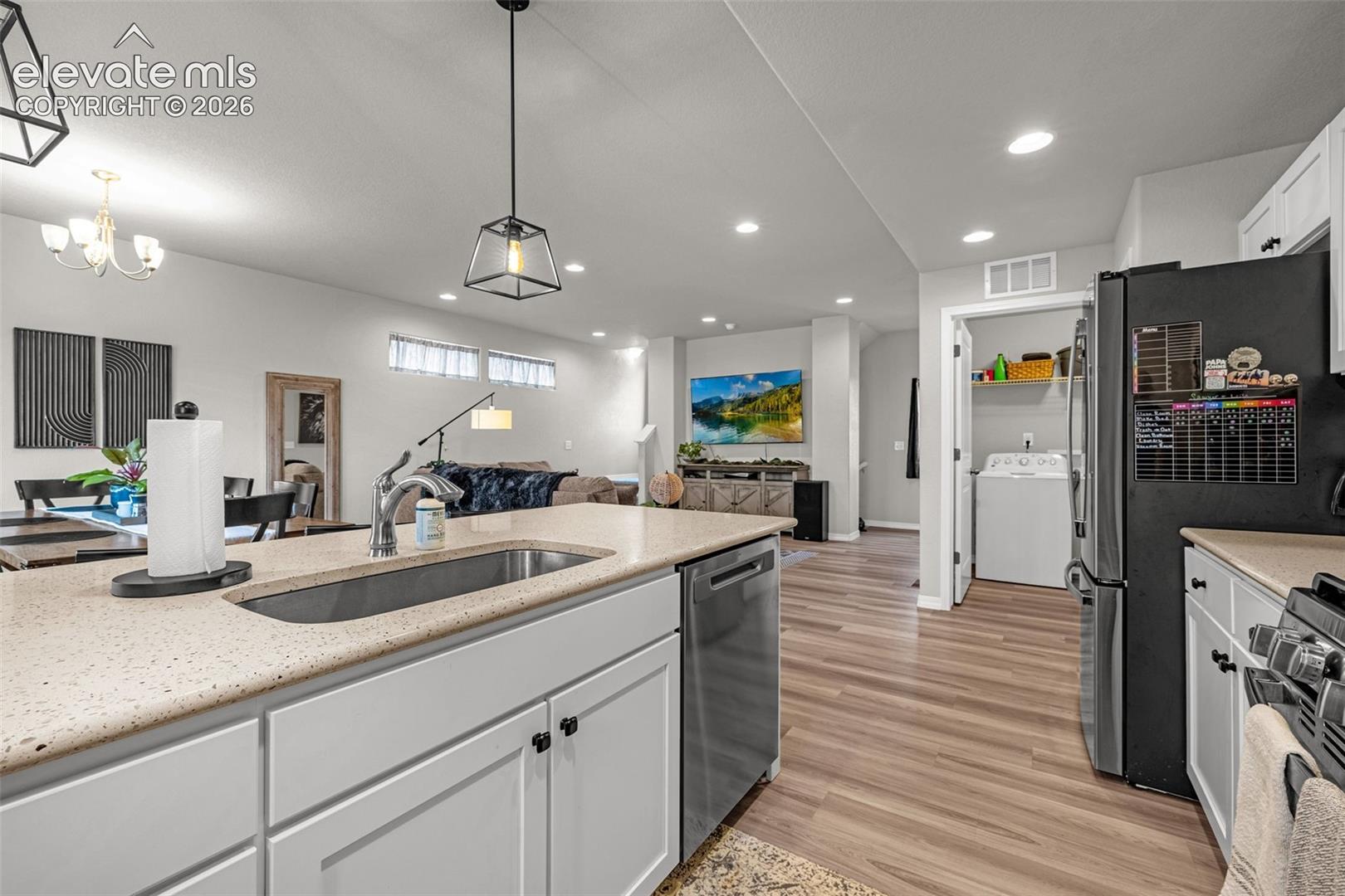 Kitchen island featuring an undermount sink, gooseneck faucet, light-toned countertop, and white cabinetry with dark hardware