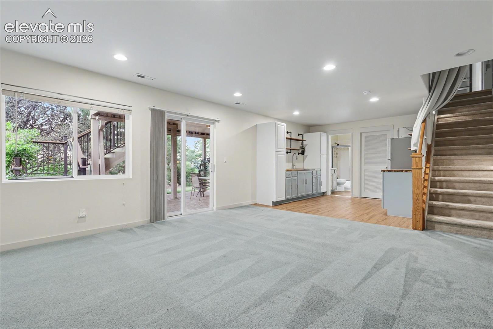 Lower-level living area with light blue carpeting, recessed lighting, and a sliding glass door leading to an outdoor patio