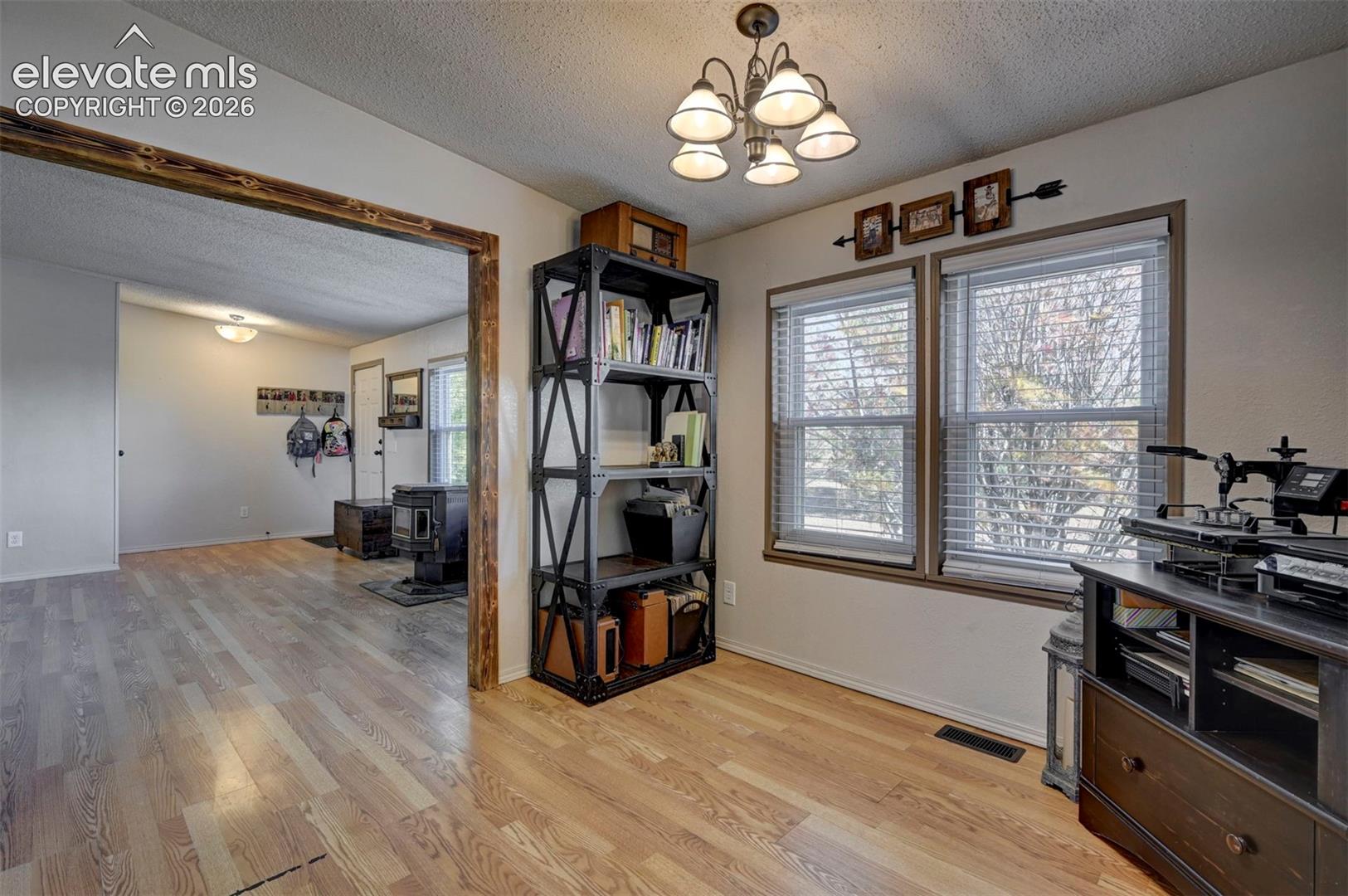 Home office with a textured ceiling, a wood stove, light wood-style flooring, and a chandelier
