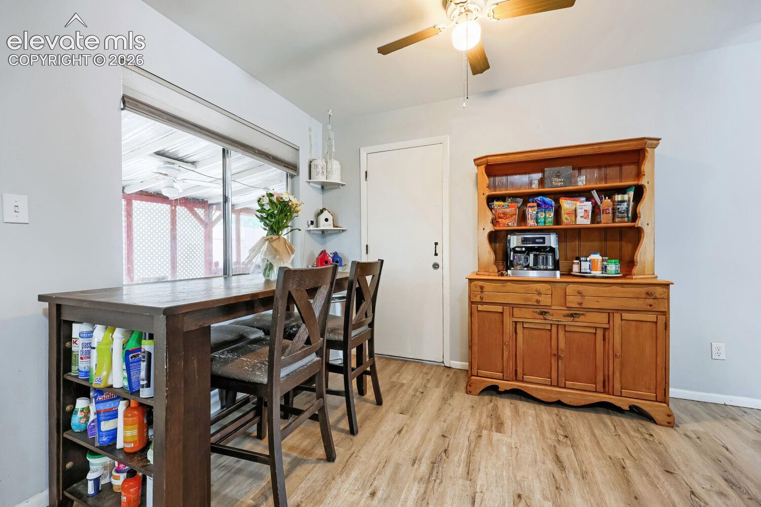 Wood-finish flooring, built-in open shelving, ceiling fan with integrated lighting, and a window with blinds