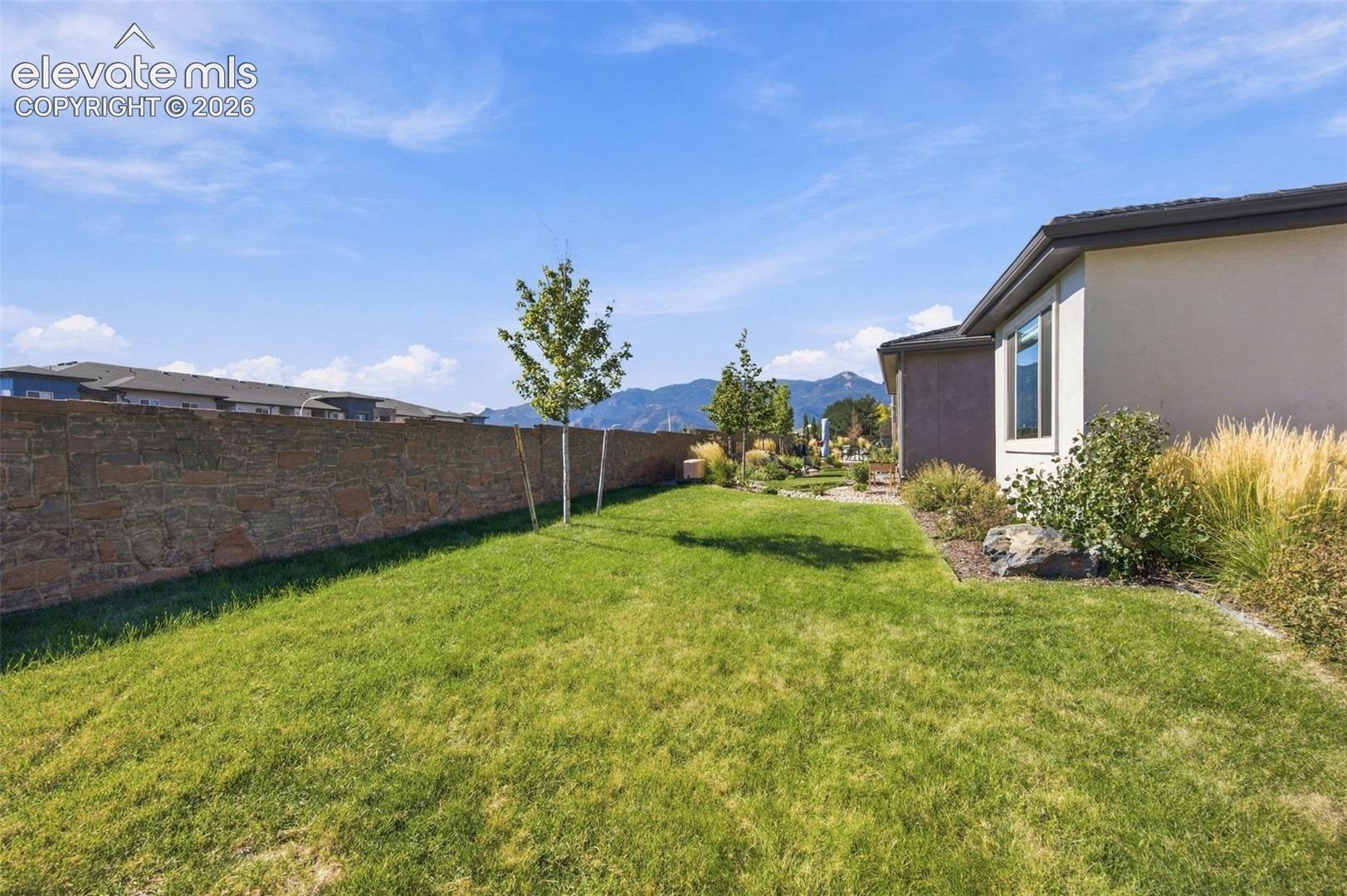 Side yard featuring a stone-veneer perimeter wall, manicured lawn, established landscaping, and mountain scenery
