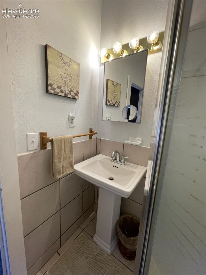 Pedestal sink with chrome faucet, integrated mirror, four-bulb vanity lighting, and wall-mounted towel bar