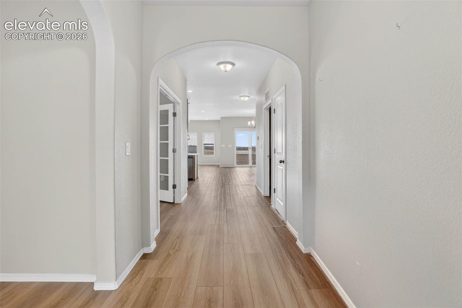 Hallway with light wood-finish flooring, arched doorways, and recessed lighting