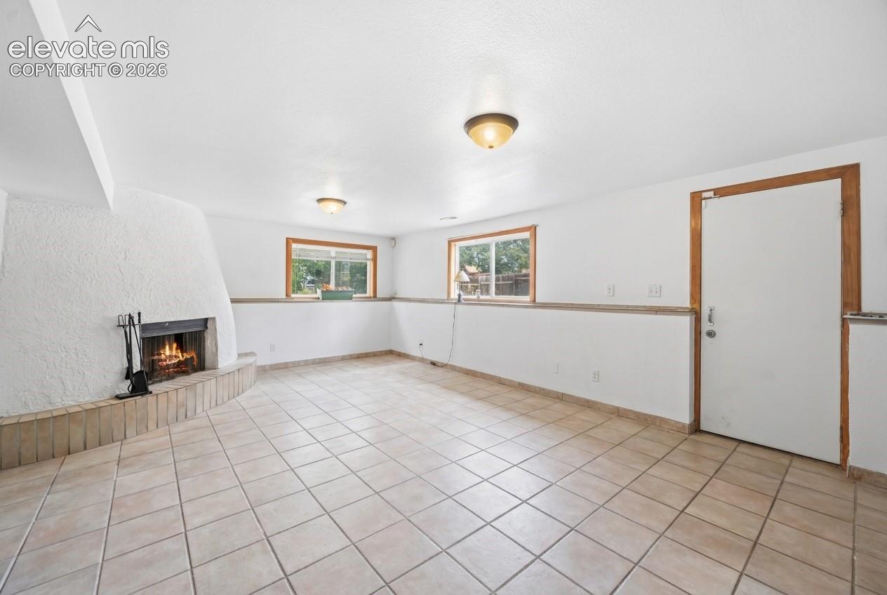Spacious room with tile flooring, a textured white stucco fireplace, and natural light from horizontal windows