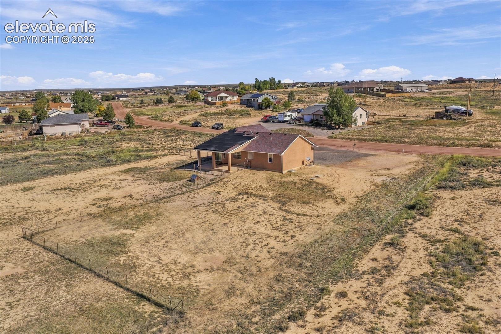 Single-story home featuring a covered patio, shingle roof, masonry exterior, and a fenced perimeter on expansive acreage