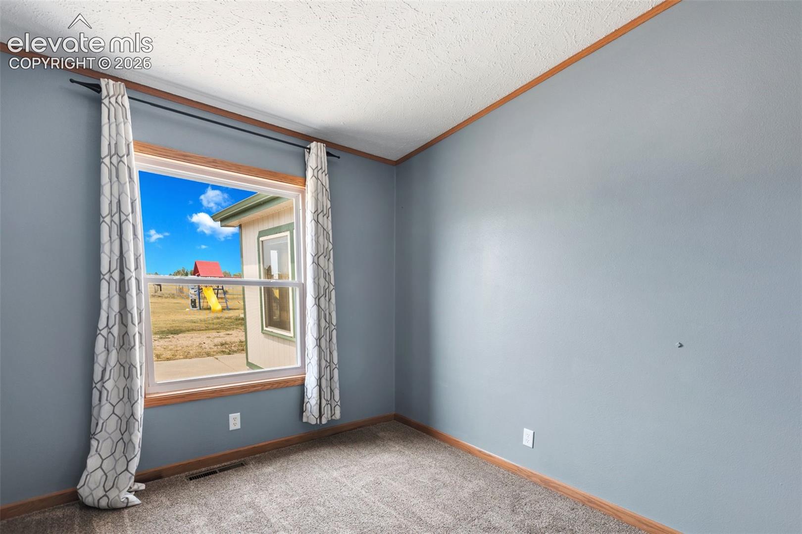 Spacious room featuring light blue walls, wood trim, and textured carpeting