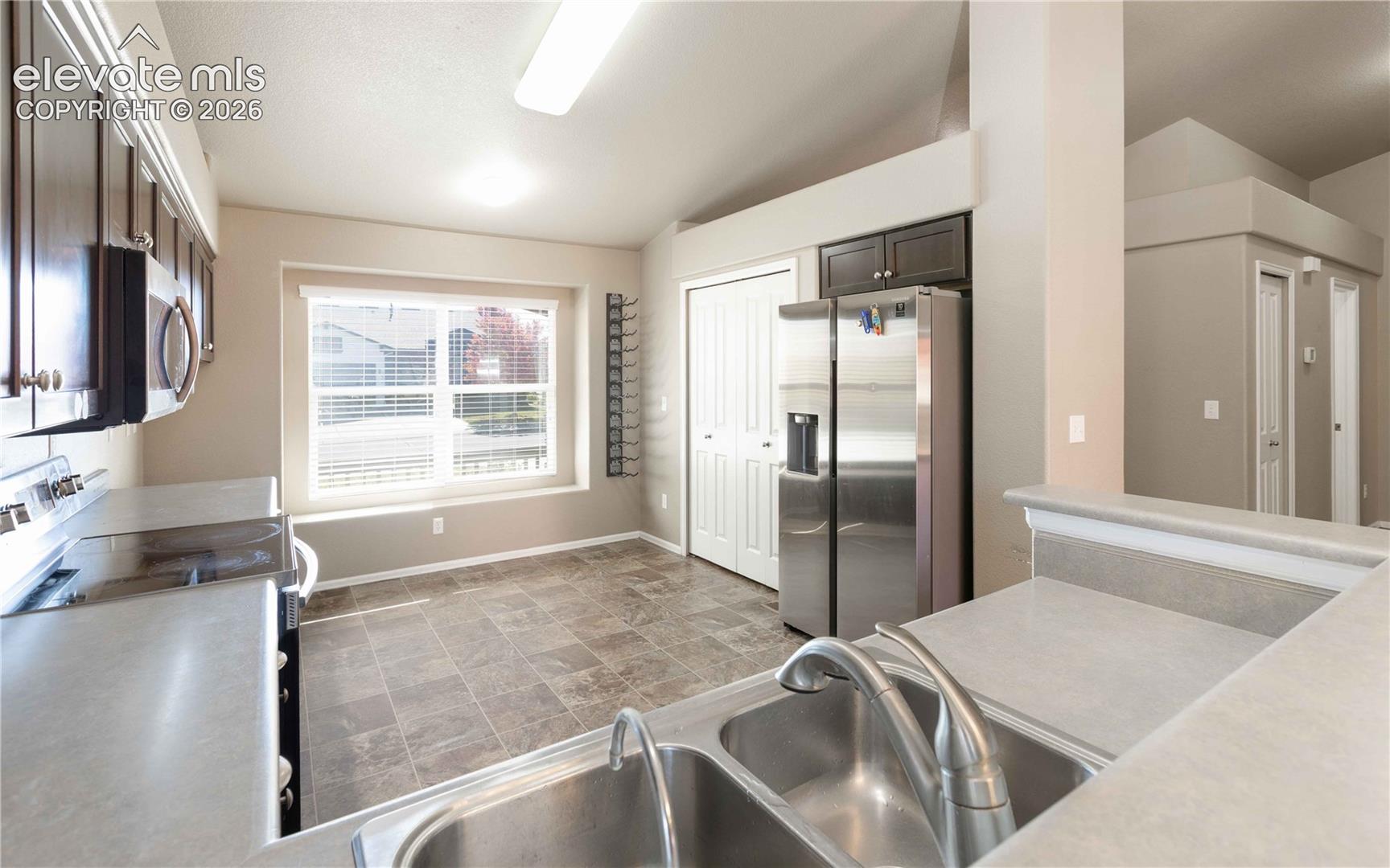 Kitchen featuring dark cabinetry, stainless steel side-by-side refrigerator, double-basin undermount sink with arched faucet, tile flooring, and a large window