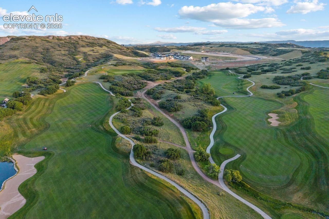 Aerial perspective of expansive golf course grounds featuring rolling fairways, sand bunkers, natural terrain with native vegetation, and winding paved cart paths