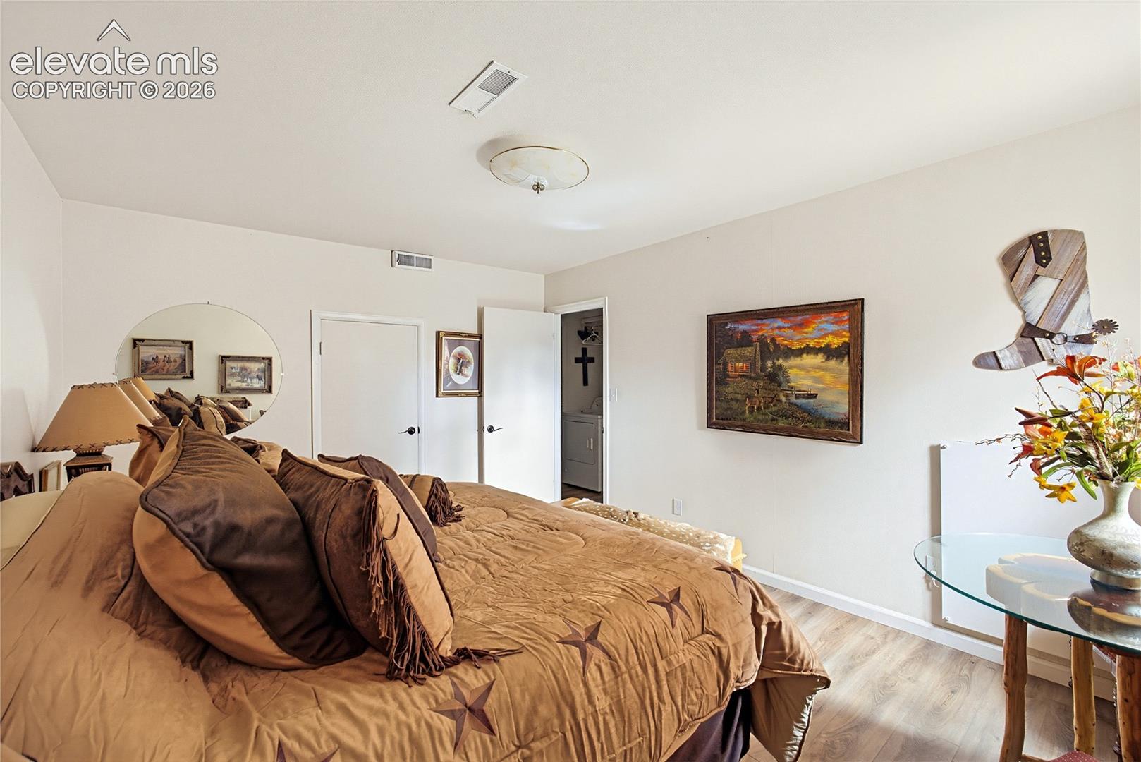 Room featuring wood-finish flooring, a circular wall-mounted mirror, and a central flush-mount light fixture