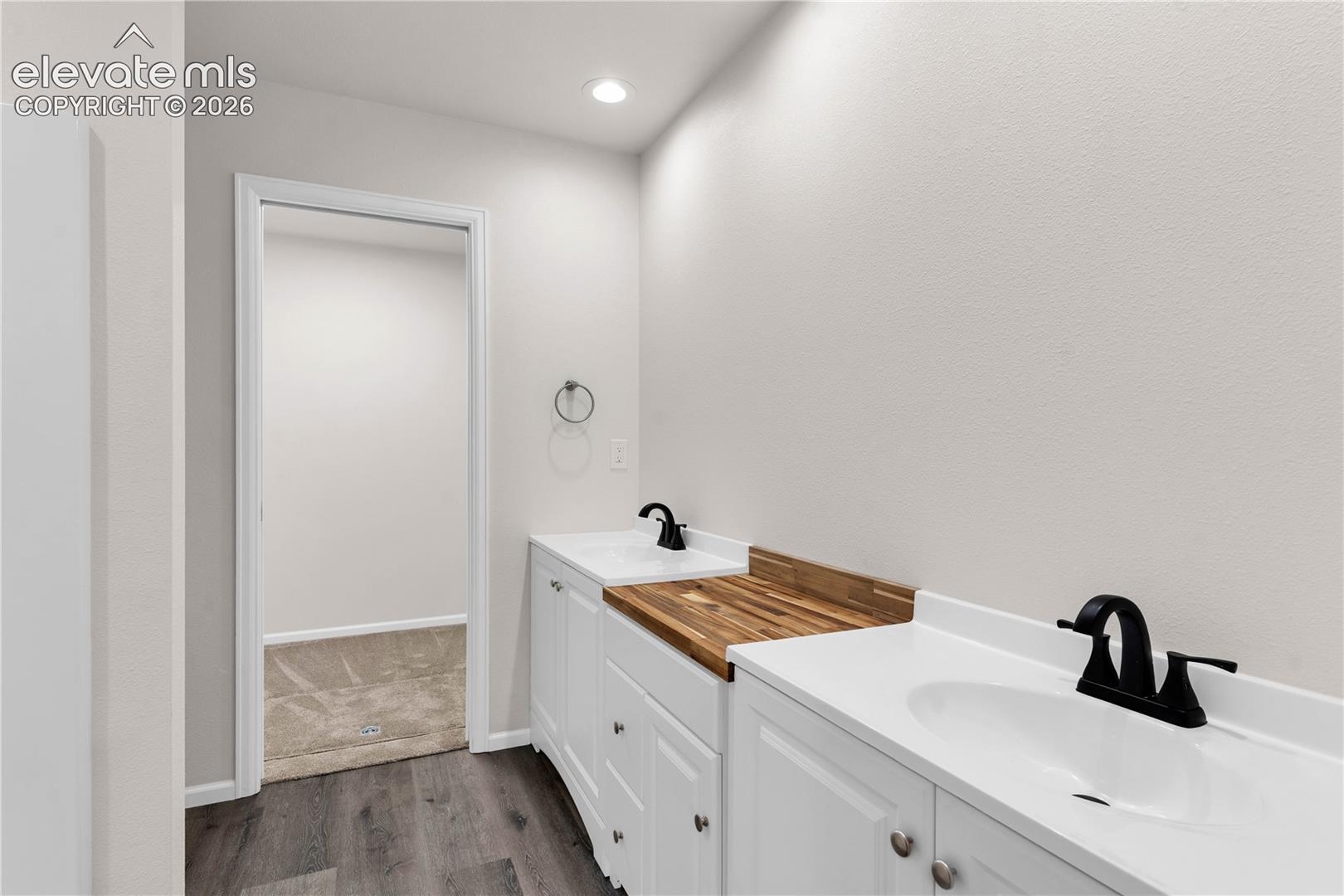 Dual-sink vanity with white cabinetry, integrated white countertops, wood-finish surface insert, and matte black hardware fixtures
