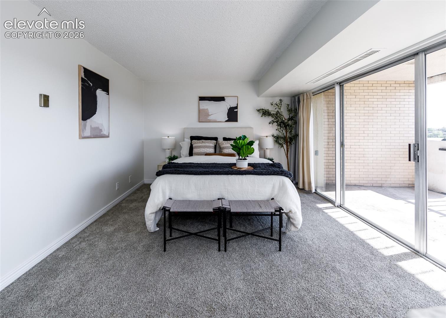 Expansive sliding glass doors, neutral carpeting, and a private outdoor balcony featuring light-toned brick masonry
