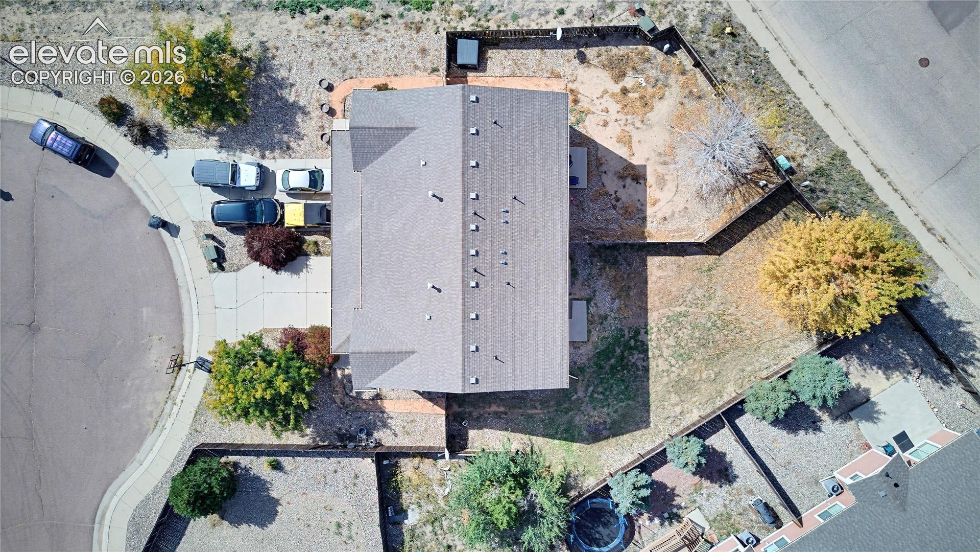 Aerial perspective of a multi-level property featuring a corner lot, paved driveway, composite shingle roof, wood-style privacy fencing, and mature landscaping