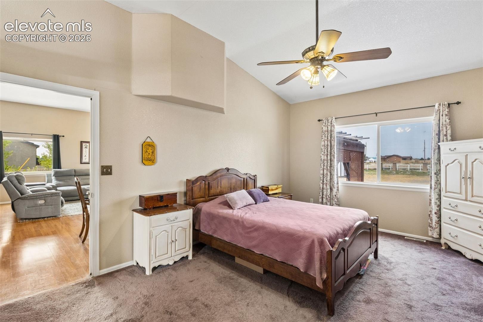 Vaulted ceilings featuring a central ceiling fan with integrated lighting, carpeted flooring, and a large horizontal window