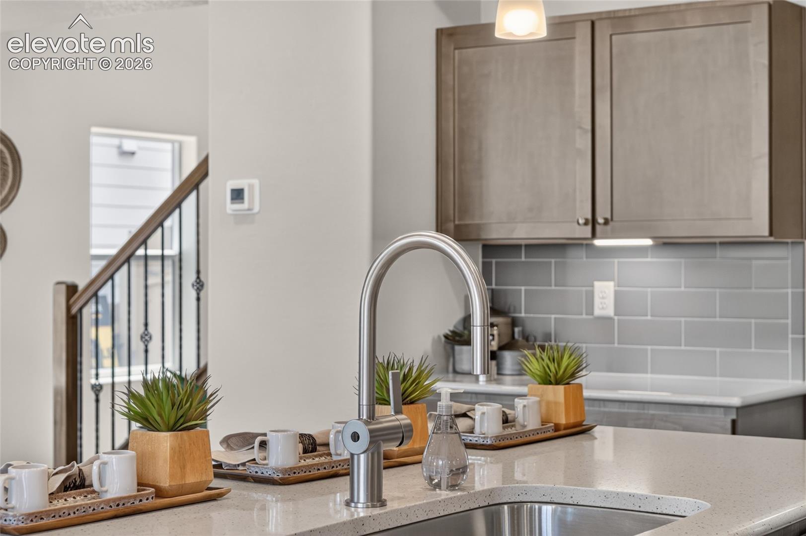 Kitchen featuring solid-surface countertops, stainless steel undermount sink with a high-arc faucet, gray subway tile backsplash, and shaker-style cabinetry