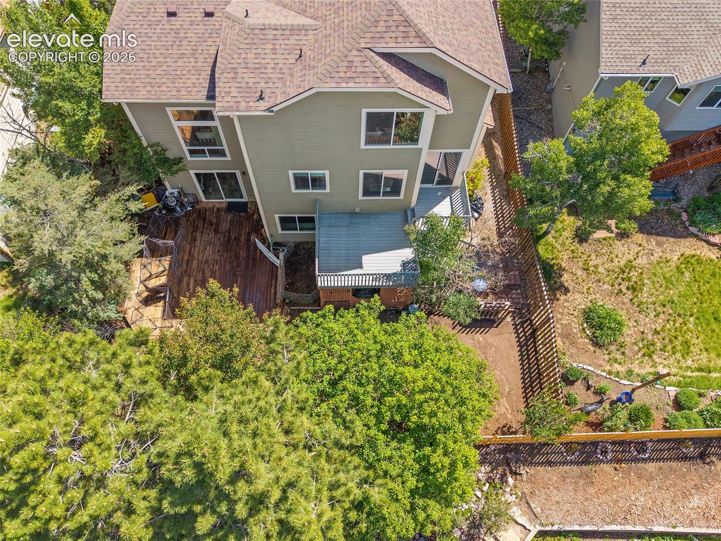 Split-level property featuring a multi-tier wood deck, a partial privacy fence, and mature trees