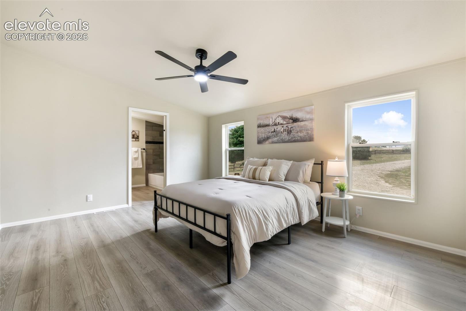 Vaulted ceiling with a black ceiling fan, wood-finish flooring, two windows, and an en-suite bathroom with a tub