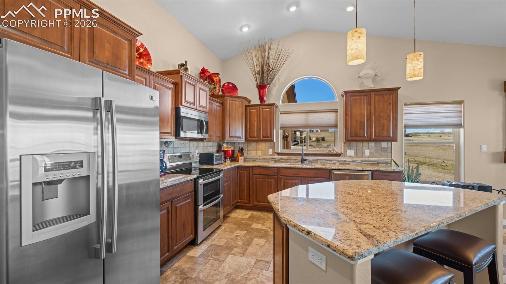 Kitchen with stainless steel appliances, a kitchen breakfast bar, hanging light fixtures, granite countertops, and a kitchen island
