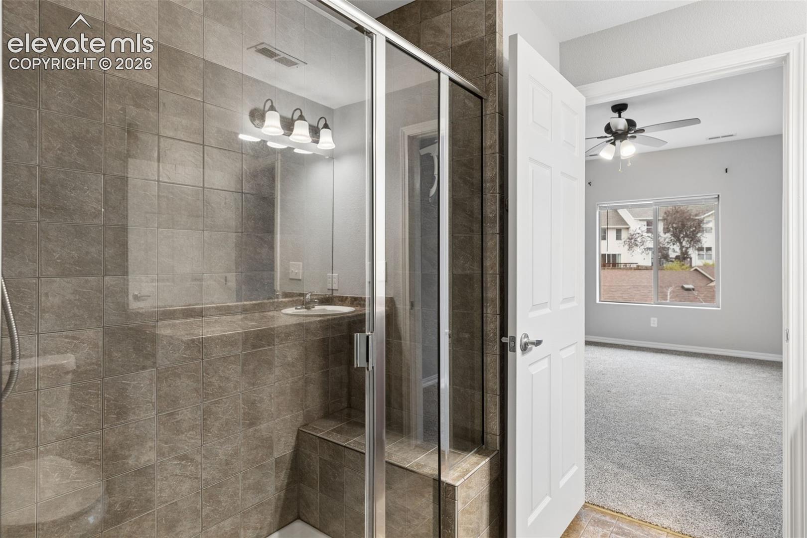 Walk-in shower enclosure featuring floor-to-ceiling tile, built-in bench seating, and glass paneling, complemented by a vanity with a tiled backsplash and recessed lighting
